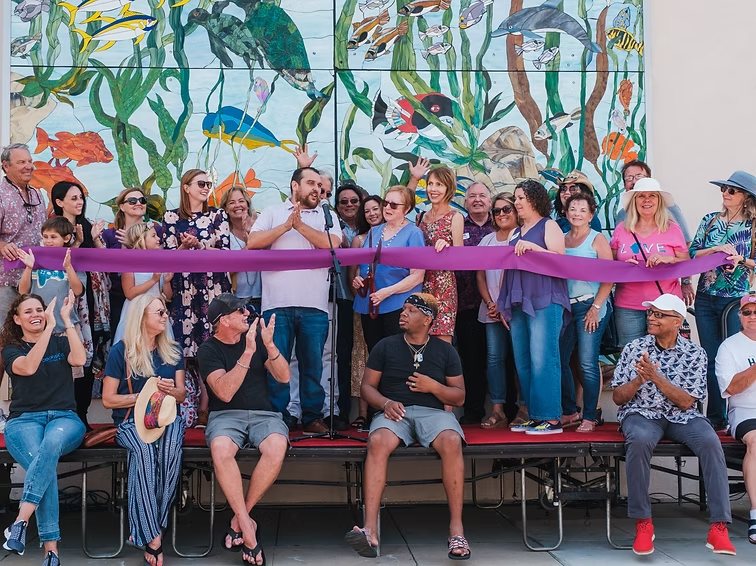 Community members at the ribbon cutting in front of a colorful ocean-themed mural